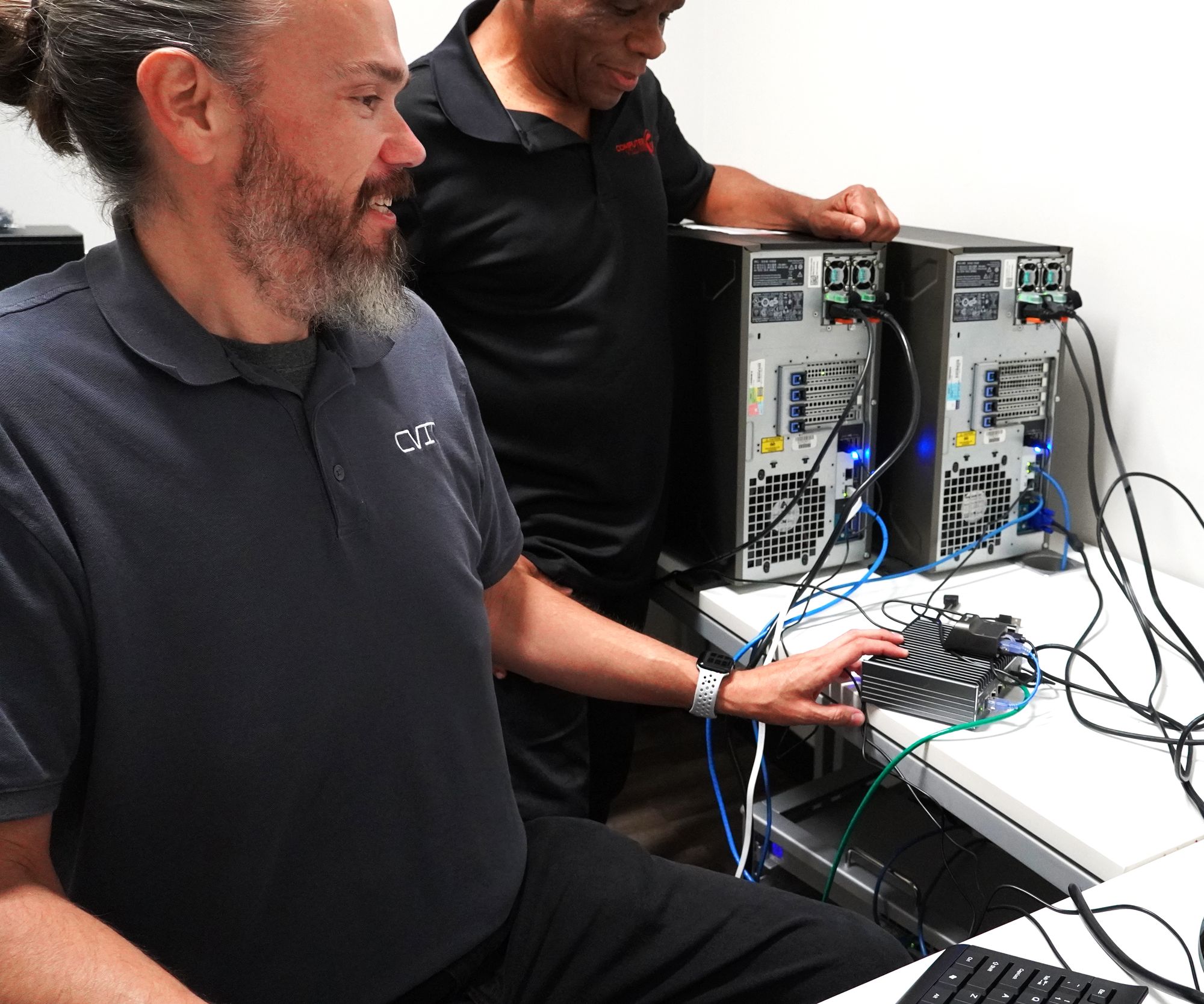 Two Computer Village technicians working on a pair of opened tower servers at the bench