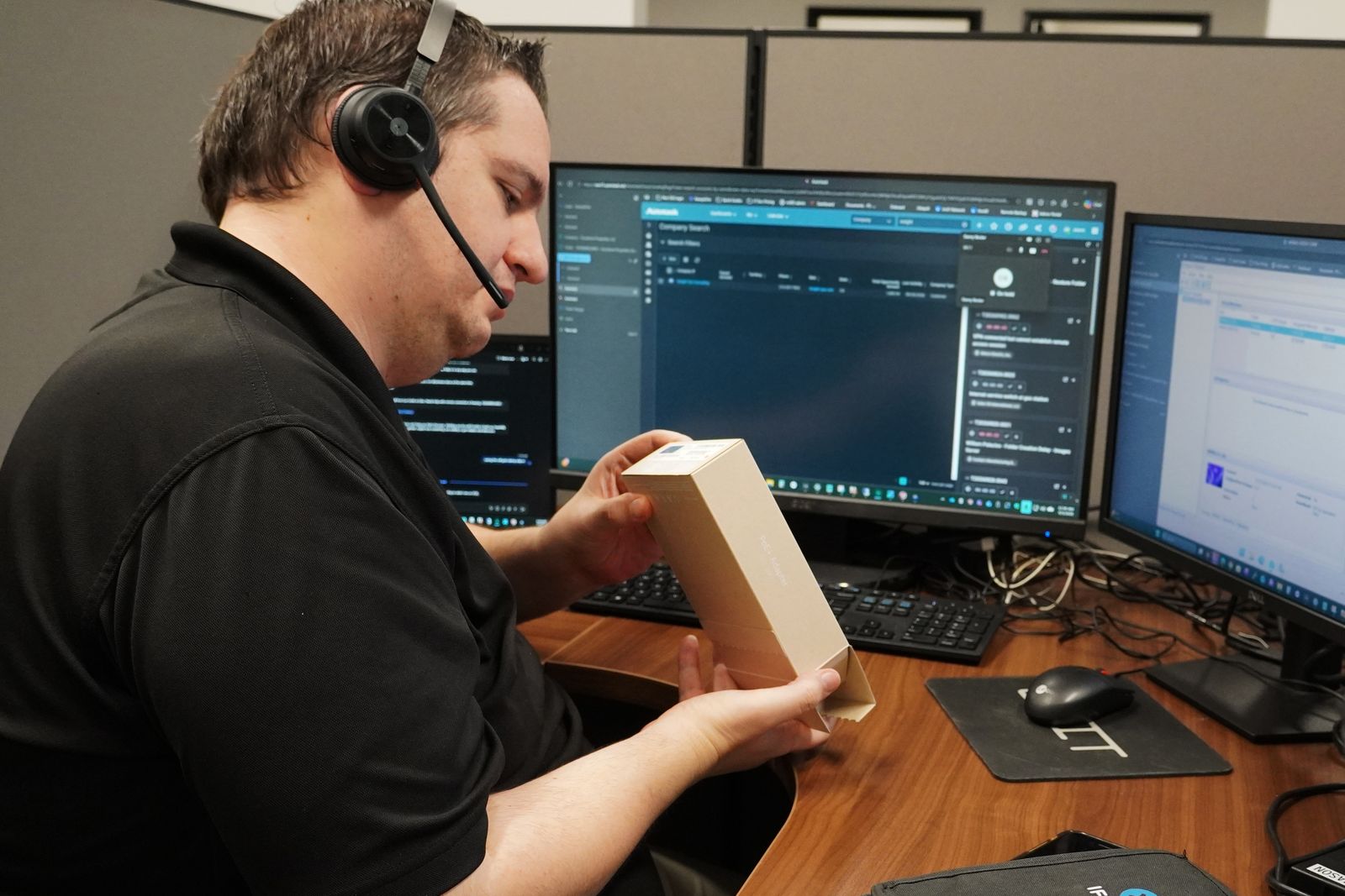 A Computer Village technician in a headset at their desk, unpacking a replacement part
