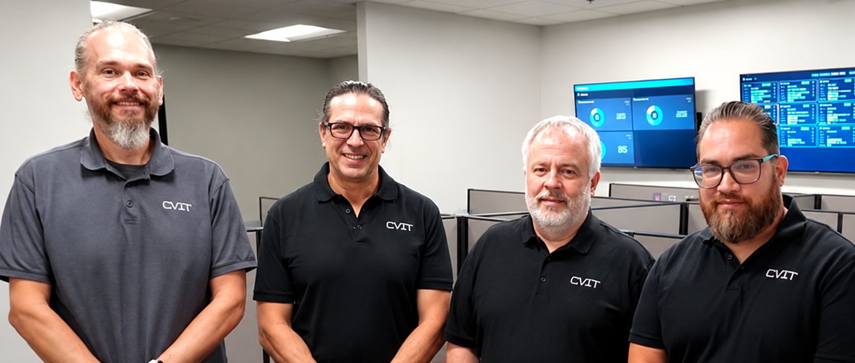 Four Computer Village staff in the operations room, the monitoring wall behind them