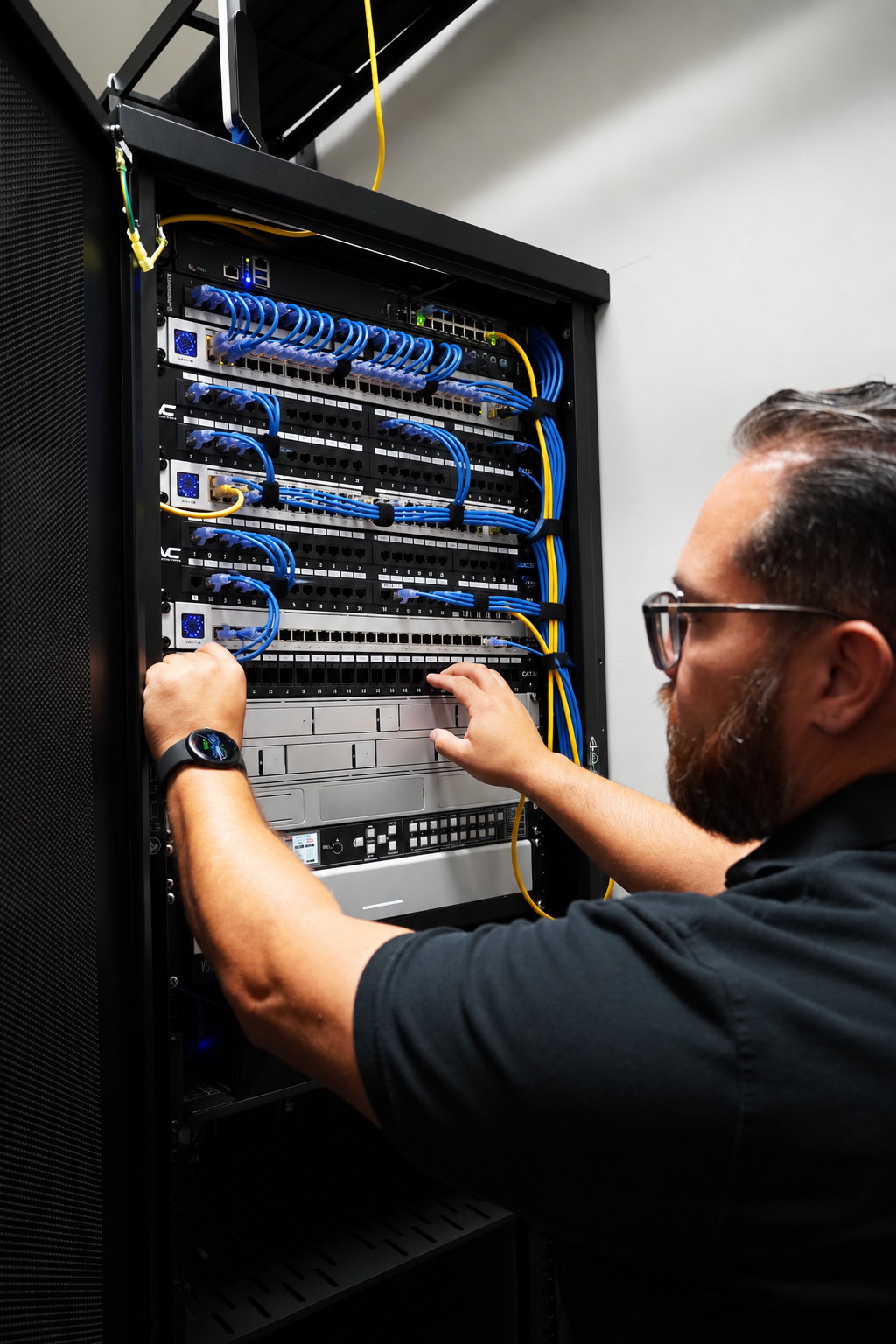 A Computer Village technician tracing a cable across a patch panel inside a network rack
